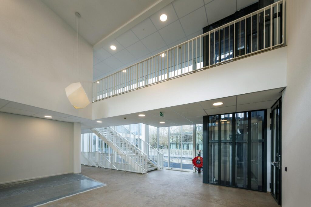 Moderne, lichte entreehal van een gebouw aan de De Cuserstraat met trap, lift en grote ramen.